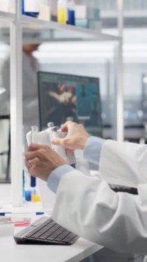 Dikey video test geliştirme uzmanı laboratuvar bankındaki mavi çözeltiyi içeren test tüpüne sıvı transfer etmek için pipet kullanır. Asyalı laboratuar mühendisi pipetleme prosedürünü kimyasalla yapıyor.