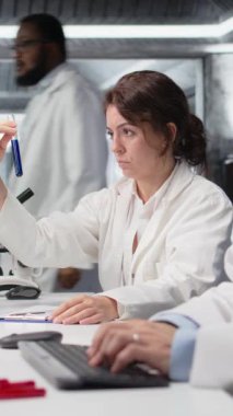 Dikey video laboratuvar kimyageri test tüpündeki sıvı örneğinin kimyasal davranışını araştırıyor. Araştırma tesisi çalışanı yeni bileşik içeren şişeyi tutuyor, ilaç geliştirme, kamera A