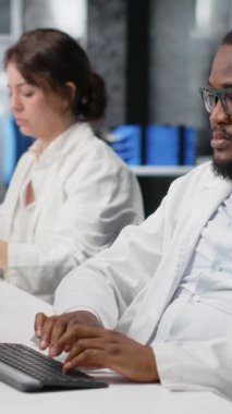 Laboratuvardaki dikey video bilimci, çalışma sırasında bilgisayar monitöründeki klinik kan değerlerini yorumluyor. Sanguine sıvısı analizi yapan araştırma tesisi çalışanı, sağlık hizmetleri raporlarına bakıyor.