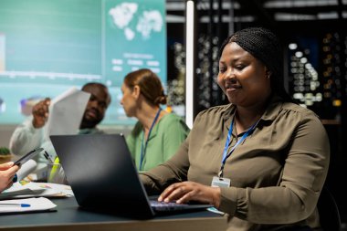 Afrika kökenli Amerikalı yönetici güncellemeleri gözden geçirmek, bir iş stratejisi oluşturmak ve net hedefler belirlemek için bir gece toplantısında dizüstü bilgisayar kullanıyor. Kadın şirket yöneticisi.