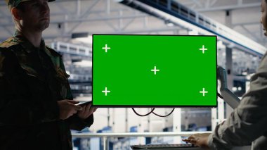 Asker ve kadın teknisyen sunucu merkezi sistemlerini yönetmek için yeşil ekran bilgisayar kullanıyor. Afrika kökenli Amerikalı kadın ve ordu komutanı, B kamerasındaki model çalışma istasyonunu kullanıyor.