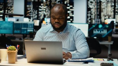 Siyah ofis çalışanı bir sandalyeye yaslanıyor ve gece yarısı dinleniyor, bir iş molasında hayal kuruyor. Tamamlanmış ve kendinden emin. Kariyer başarısını ve şirket başarılarını yansıtıyor..