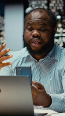 Dikey Video Siyah çalışanı gece geç saatlerde telefon web telekonferansında sohbet ediyor, verimlilik için dijital bir tartışmaya girişti. Hissedarlarla etkileşim. Şirkette ağ oturumu