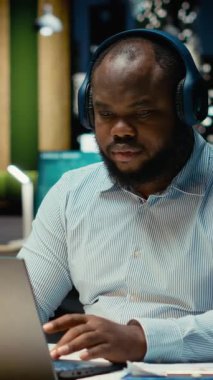 Dikey Video Afrikalı Amerikalı adam gece geç saatlerde müzik eşliğinde günlük işlerle uğraşıyor. Odaklanma ve verimliliğe yardımcı olmak için odak seslerinden ilham alıyor. Erkek.