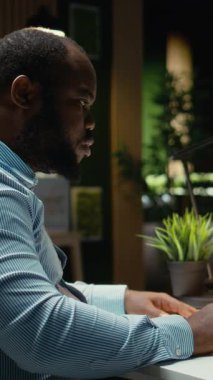 Dikey Video Siyah iş danışmanı gece geç saatlere kadar dokümanları düzeltip dizüstü bilgisayarda raporlar yazıyor. Şirket amaçlarına uygun bir özet hazırlamak ve strateji tasarlamak. Kamera.