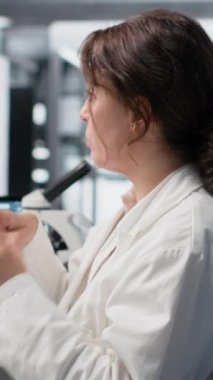 Dikey video laboratuvar teknisyeni araştırma belgeleri için laboratuvar deneylerinden gözlemler yazıyor. Araştırma tesisi uzmanı not alıyor, klinik raporlar hazırlıyor.