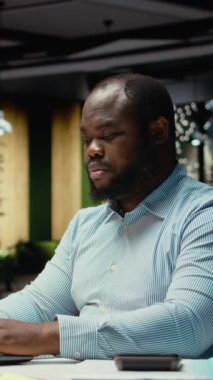 Dikey Video Afrikalı Amerikalı işçi mesai bitiminden sonra ofiste yalnız olduğunu fark ediyor ve diğer iş istasyonlarına bakıyor. Çalışanlar gece geç saatlere kadar çalışarak iş amaçlarına ve amaçlarına ulaşırlar.