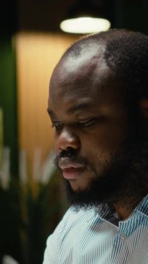 Dikey Afrikalı Amerikalı adam dizüstü bilgisayarda bilgi yazıyor ve raporları kontrol ediyor, yeni bir iş hedefi veya hedefi için verileri düzeltiyor ve gözden geçiriyor. Mesai sonrası şirket yönetimi. Kamera B.