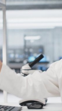 Dikey video laboratuvar kimyageri test tüpündeki sıvı örneğinin kimyasal davranışını araştırıyor. Araştırma tesisi çalışanı yeni bileşik içeren şişeyi tutuyor, ilaç geliştirme, kamera B