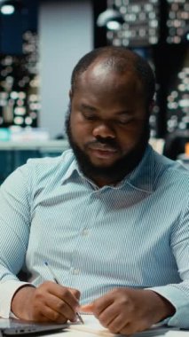 Dikey Video Siyah ofis çalışanı bir hata yaptıktan sonra bir kağıt parçasını yırtıyor, görevini öfkeyle yeniden başlatıyor ve sayfa sayfasını yırtıyor. Hoşnutsuz adam yazım hatası yazar.