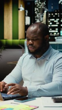 Dikey Video Siyah ofis çalışanı, mesai saatleri dışında akıllı telefonları kontrol ederek, gece mesaisinde fazla mesai yaparken sosyal hizmetlerle bağlantılı bir bildirimi kontrol ediyor. Genç adam mesajları okuyor. Kamera A