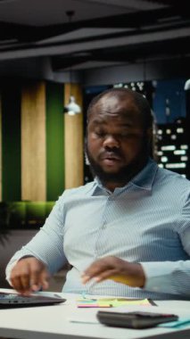 Dikey Video Afrikalı Amerikalı ofis çalışanı dizüstü bilgisayarına yapışkan bir not bırakıyor, yapılacaklar listesinden bir görevi hatırlamaya çalışıyor. Gece çalışıyor ve ertesi sabah için not bırakıyordu.