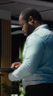 Dikey Afrikalı Amerikalı adam bir belgeyi düzelterek ders kitabına yazmadan önce dizüstü bilgisayardaki raporlardan ana fikirleri ayıklıyor. Gece geç saatlerde belgelendirme uzmanı. Kamera B.