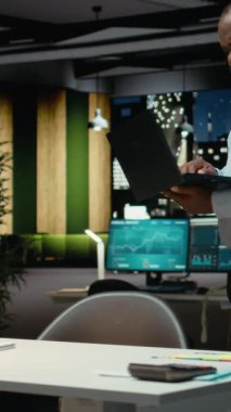 Dikey Afrikalı Amerikalı adam bir belgeyi düzelterek ders kitabına yazmadan önce dizüstü bilgisayardaki raporlardan ana fikirleri ayıklıyor. Gece geç saatlerde belgelendirme uzmanı. Kamera A.