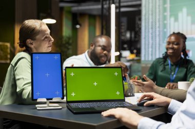 Çok ırklı analistlerden oluşan bir ekip, mesai saatleri dışında bir şirkette fotokopi alanı ile işbirliği yaparak güncellemeleri tartışıyor ve belgeleri değiş tokuş ediyor. Geliştirme sonuçlarını tahmin etmek için diyagramlar.