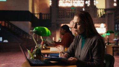 Entelektüel olgun bir kadın üniversitedeki dizüstü bilgisayarından akademik metni kopyalıyor, klasik çalışma odasında oturuyor ve çevrimiçi dokümanları tamamlıyor. Resmi öğrenim yoluyla eğitim.