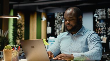 Afro-amerikan ofis çalışanı laptopuna yapışkan bir not bırakıyor, yapılacaklar listesinden bir görevi hatırlamaya çalışıyor. Gece çalışıyor ve ertesi sabah için not bırakıyordu..