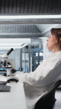 Dikey video yorgun laboratuvar bilim adamı gözlerini ovalıyor, genetik işaretleri PC kullanarak değerlendirmekten yoruldu. Bilgisayar masasındaki DNA iplikçikleri, iç çekiş ve kamera A 'dan yorgun düşmüş bir uzman.