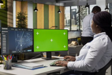 Mühendis enerji denetim bulgularını tanımlamak için yeşil ekrandaki elektrik şebekesi verilerini inceliyor. İşçi model bilgisayardaki iletim kulesi verimlilik ölçüm analizi paneline bakar