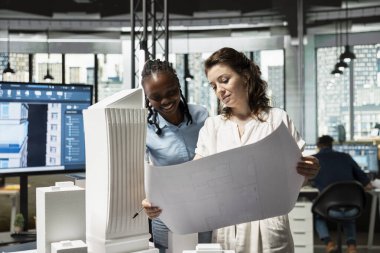 Emlak çeşitliliği ekibi inşaat planlarını analiz ediyor, imar düzenlemelerini ve konut projesi için 3D modellerle mühendislik detaylarını inceliyor. Gelişim için akıllı şehir vizyonu.