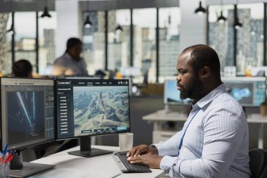 Ar-Ge uzmanı, sürdürülebilir altyapıyı güçlendirmek için elektrik hatlarını ve VAWT türbini tasarımlarını analiz ediyor. Afrika kökenli Amerikalı adam gelişmiş teknoloji rüzgâr çiftliği planlarını ve elektrik şebekelerini modelliyor.