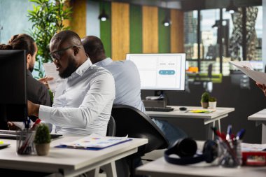 Modern ofiste işbirliği yapan, proje planlama, performans ölçümleri ve rapor paylaşımına odaklanan çeşitli çalışanlar. Öngörü için işadamları verileri gözden geçirir.