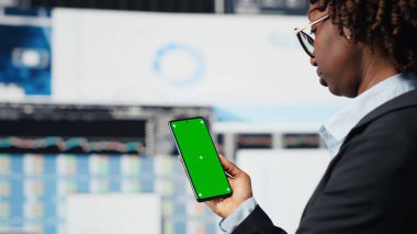 Yönetici tarafından kullanılan yeşil ekran model telefon beyin fırtınası yaparak iş piyasası grafiklerini değerlendiriyor. İş kadını, izole ekran kroma anahtar telefonu B kamerasındaki mali raporları ve veri grafiklerini analiz ediyor.