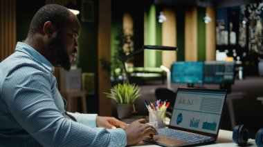 Siyah iş danışmanı gece geç saatlere kadar dokümanları düzeltip dizüstü bilgisayarda rapor yazıyor. Bir özet oluşturuluyor ve şirket hedefleri ile hizalamak için strateji tasarlanıyor.