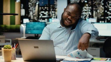 Erkek çalışan, gece geç saatlerde uzaktan sohbet için telefonla ortağını arıyor. Telefon hattındaki işbirliği sırasında gülümsüyor ve görüşünü paylaşıyor. Adaptasyon ve özen.