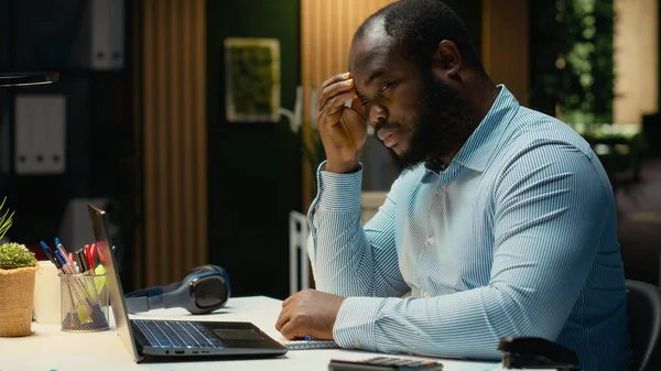 Siyahi sorunlu işçi, yoğun iş yükü veya başarısızlık nedeniyle yorgunluk ve rahatsızlığını ifade ederek, hayal kırıklığı ve yorgunluk içinde başını ovuşturuyor. Öfkeli adam baskı altında hisseder..