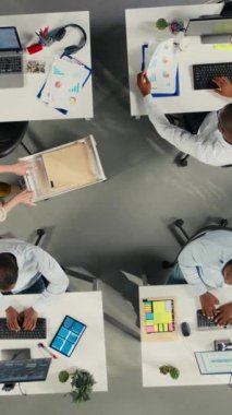 İş yerindeki arşivlenmiş dosyaları inceleyen, grafikleri ve analizleri inceleyen meslektaşları dikey Görüntü Üst görünümü yakınlaştır. Çalışanlar proje ilerlemesini tartışıyor, yazma ve veri görselleştirmesini raporluyor