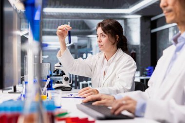 Analitik kimyager steril laboratuvar ortamında test tüpü kullanarak kimyasal örnek özelliklerini araştırıyor. Araştırma tesisi çalışanı yeni bileşik içeren şişeyi tutuyor, ilaç araştırmaları yapıyor.