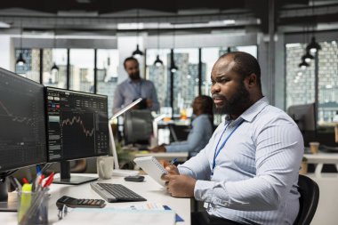 Borsa Ölçümlerini takip eden tüccar ve PC 'deki ticaret yazılımını kullanarak siparişleri yerleştiriyor. Komisyonculuk bürosundaki Afrikalı Amerikalı adam müşteriler adına menkul kıymetleri takas ediyor.