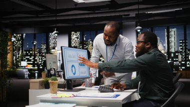 Afrika kökenli Amerikalı işçiler geceleri görev çözmede birbirlerine danışırlar, aylık raporları tamamlarlar ve verimlilik için KPI verilerini incelerler. Başarı için işbirliği.