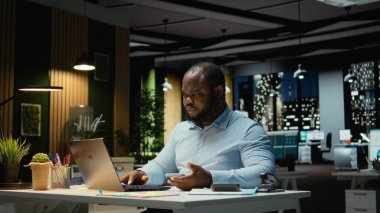 Siyahi işadamı cep telefonundan iç çekip mesajları kontrol ediyor, modern ofisteki bir tebligat yüzünden dikkati dağıldıktan sonra tükenmiş ve kaşlarını çatmış hissediyor. Geceleri işyeri sorunları.