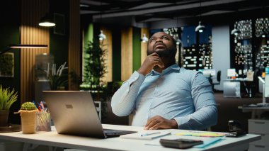 Afrika kökenli Amerikalı erkek, bir iş stratejisi ikilemi üzerine kafa yoruyor, gelecekteki sonuçlar için yaratıcı kavramları yansıtıyor. Organizasyon sorununa çözüm bulmak için derin düşüncelere dalmak.