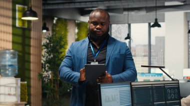 Afrika kökenli Amerikalı bir ofis çalışanı iş kaynakları ve performans raporlarını incelemek için tablet kullanır, çok uluslu bir şirket alanındaki hava tahminleri için bilgi verir. Kamera B.