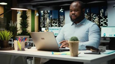 Siyah iş adamının portresi, not defterine veri yazmadan önce, geceleri ofiste oturmadan önce eleştirel düşünme ve düzeltme yapar. Önemli fikirleri fazla mesai için belgeliyorum. Kamera A.