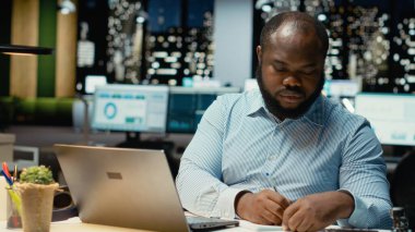 Siyah adam temel fikirleri kağıda döküyor, dizüstü bilgisayarda okuyor, geceleri görev planları yapıyor ve programlıyor. Hedefleri yansıtan bir sunum için el yazısıyla not alıyor.