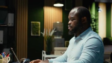 Siyahi bir danışman, gece geç saatlere kadar ayakta kalıp kurumsal işlerle ilgilenmek için bir fincan kahvenin tadını çıkarıyor. Geceleri kafein içeceğiyle düzeltme ve yazma. Kamera B.