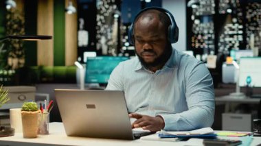 Siyah sert adam odak müziğine ve ofiste esnemeye ara veriyor. Mesai saatleri dışında çok çalışıyor ve uyanık kalmak için çabalıyor. Fazla mesai nedeniyle uykusuzluk ve gerginlik. Kamera B.