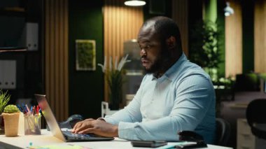 Kızgın Afro-Amerikalı adam sinirleniyor ve işlerini bitiremiyor, tükenmişlik ve zihinsel yorgunlukla uğraşıyor. Adam mesaiden sonra çalışıyor ve yorucu zorluklarla yüzleşiyor. Çok gergin bir erkek. Kamera B.