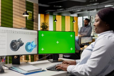 Mühendis, sürdürülebilirlik ölçümlerini geliştirerek türbin bileşenlerini analiz etmek için yeşil ekran modelleme bilgisayarı kullanıyor. İşteki kadın, salınımları azaltmak ve temiz enerji üretmek için krom anahtardaki türbin parçalarına bakıyor.