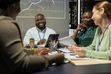 Afrika kökenli Amerikalı denetçi sermaye fonu tahminleri sunuyor ve toplantı sırasında iş haritaları üzerinde veriler sunuyor, bir kalkınma projesi için kaynak tahsisini yönetiyor. Brifing konferansı.