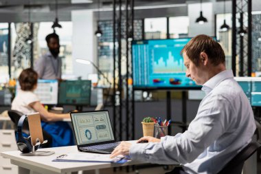 Erkek ofis çalışanı çevrimiçi belgeler ve veri yönetimine odaklanarak dizüstü bilgisayardaki sunumlara hazırlanıyor. Kafkasyalı iş adamı bütçesi ve kurumsal işyerindeki verimliliği artırma.