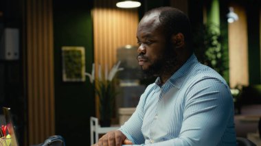 Gergin bir siyah adam yoğun iş yükü yüzünden sinirlenir, saatler sonra hüsran ve rahatsızlık içinde çalışır. Endişeli huzursuz çalışan karanlık ofiste bunalıyor..