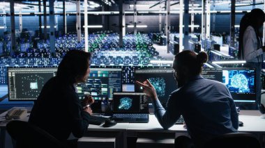 Veri merkezinde kıdemli programcı ve iş arkadaşı üretici yapay zeka yardımıyla kodlama yapıyor. Yapay zekaya baskı yapan takım arkadaşları görevleri çözmek için büyük dil modeli, kamera A