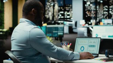 Erkek ofis çalışanı geceleri rakamları ve mali veri ölçümlerini kontrol ediyor, güncellemeleri belgeliyor ve yaklaşan iş etkinliklerinin gündemini düzenliyor. İdari görevler. Kamera B.