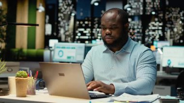 Afrika kökenli Amerikalı bir adam, gece ofiste oturup not defterine veri yazmadan önce eleştirel düşünme ve düzeltme yapıyor. İşçi önemli fikirleri belgeliyor. Kamera B.