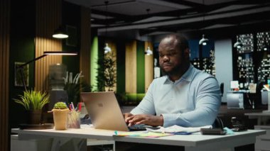 Afrika kökenli Amerikalı bir adam, gece ofiste oturup not defterine veri yazmadan önce eleştirel düşünme ve düzeltme yapıyor. İşçi önemli fikirleri belgeliyor. Kamera A.